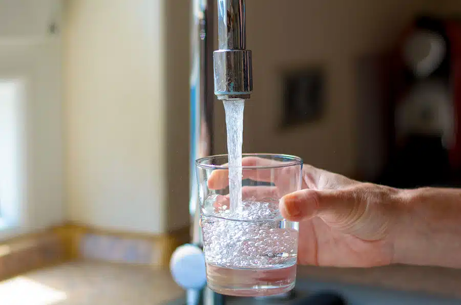Person filling water cup in residential kitchen in Denver, CO.
