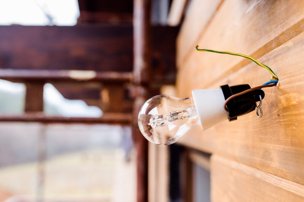 Light bulb hangs on wires on wooden wall.